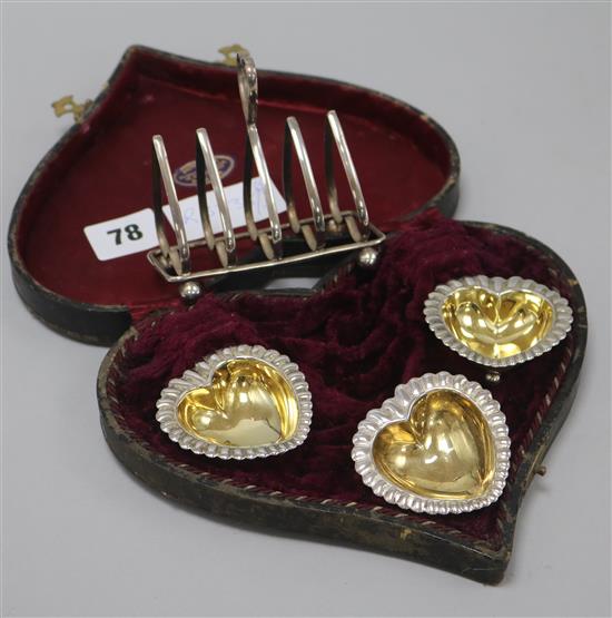 Three silver plated heart shaped salts and a toast rack